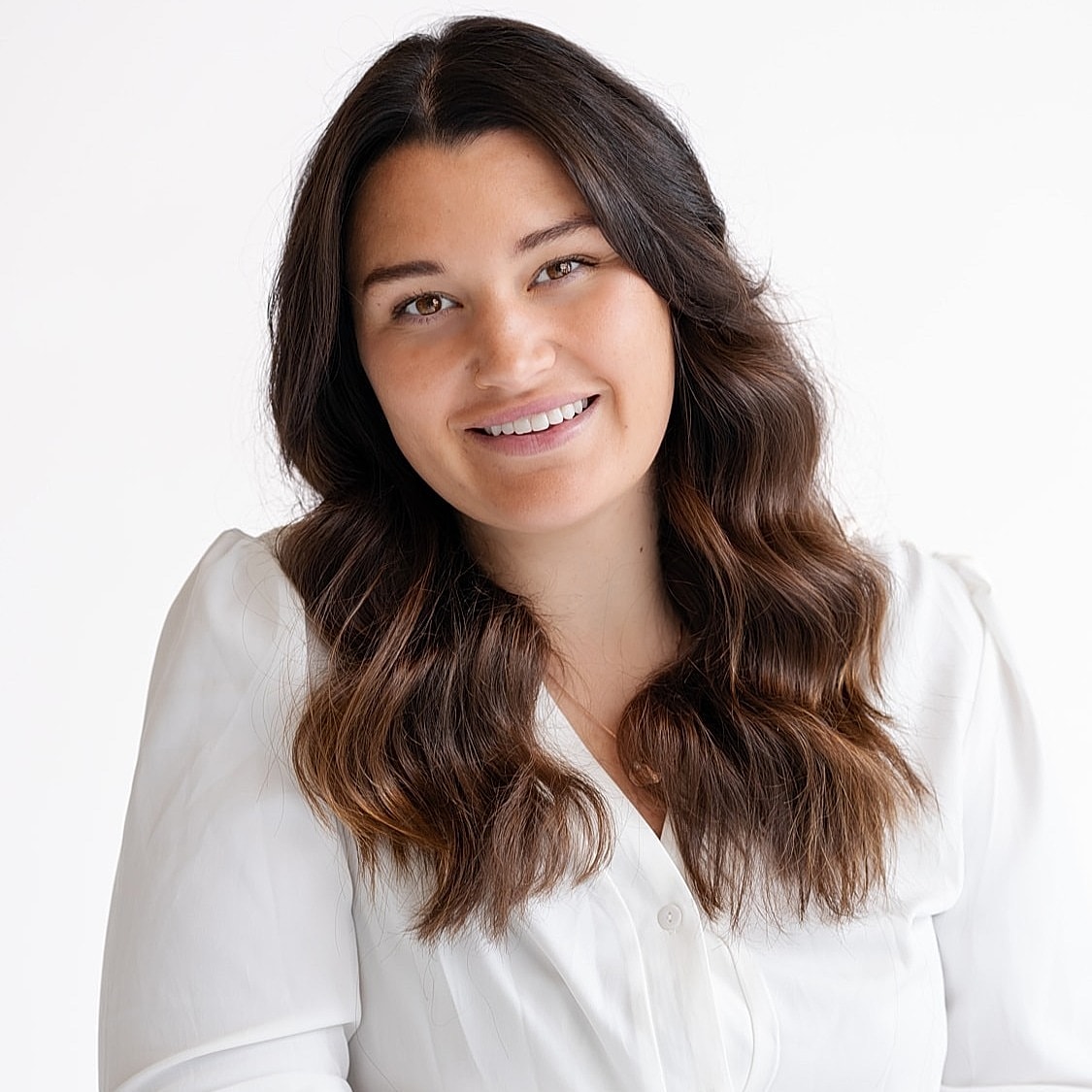 Woman smiling in white blouse, seated casually.