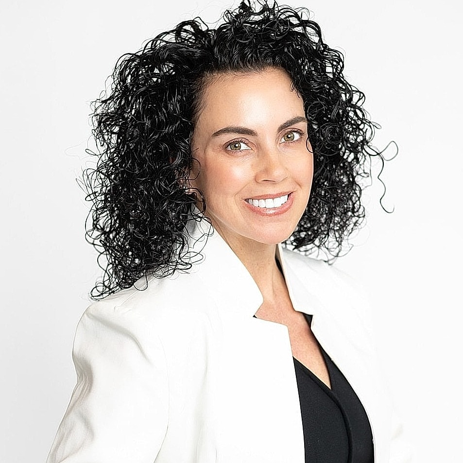 Smiling woman with curly hair in white blazer.