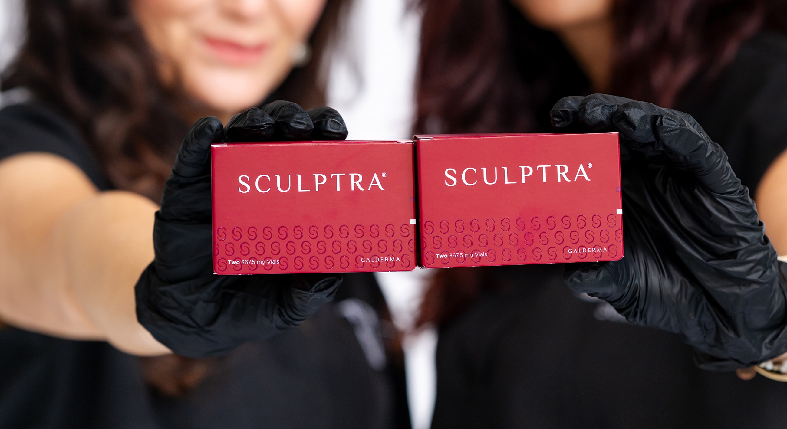 Two Sculptra boxes held by gloved hands.