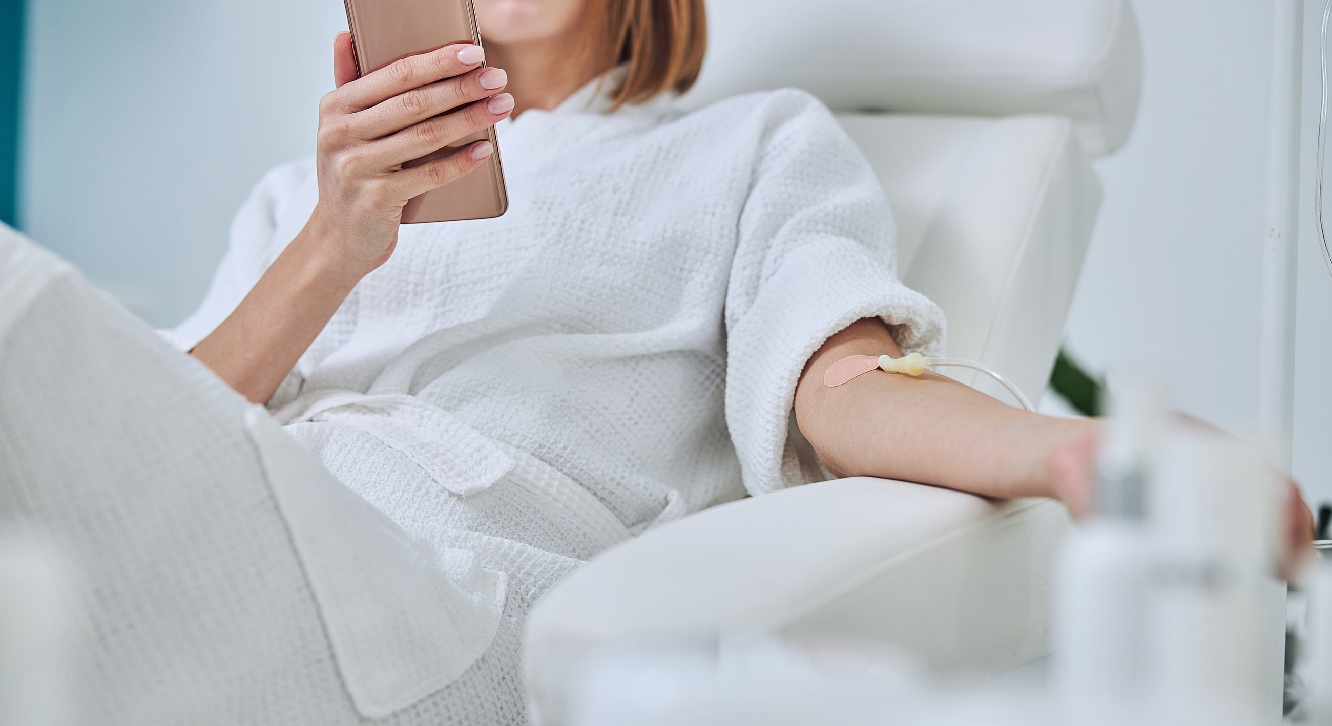 Woman in robe using phone during infusion therapy.